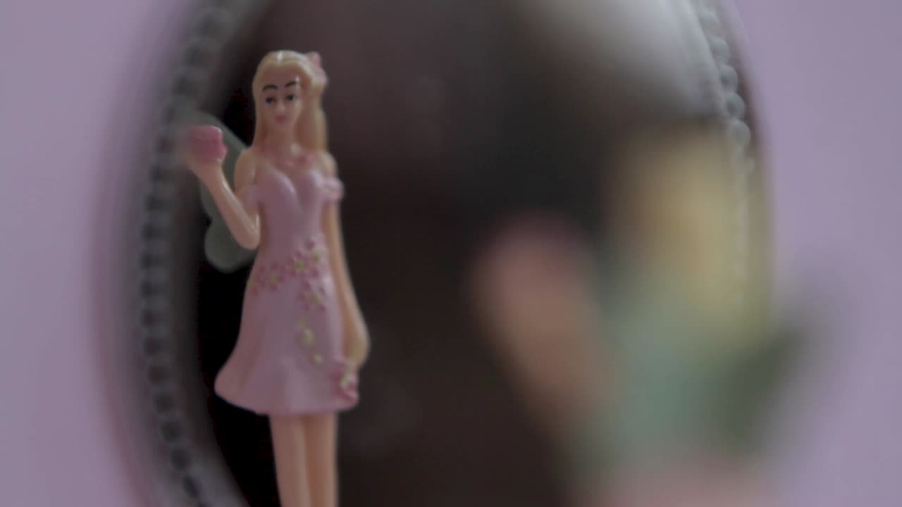 Close-up de uma boneca fada em miniatura em foco suave com movimento giratório, em um fundo pastel suave.