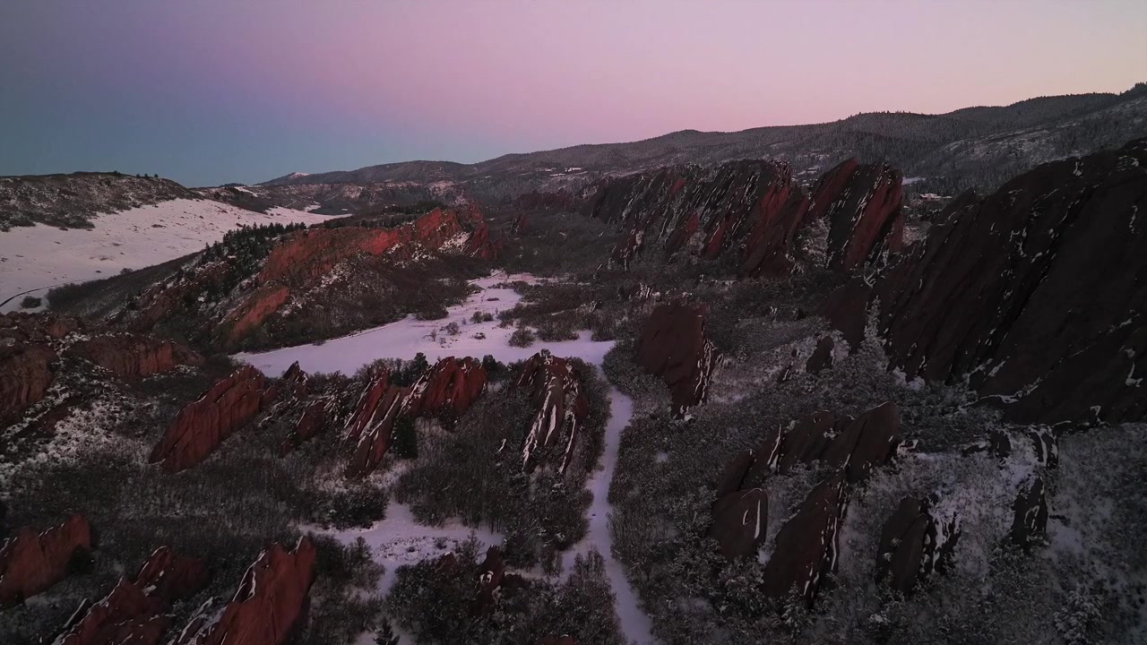 Ripresa aerea con drone al tramonto del sentiero Fountain Valley coperto di neve nel Roxborough State Park, con il punto di riferimento di arenaria frastagliata delle Red Rocks, Sterling Ranch, Littleton, Denver, Front Range e l'Arrowhead Golf Course in Colorado.