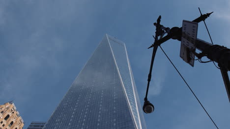 one world trade center breaching blue sky and wispy clouds with nyc signpost, low angle