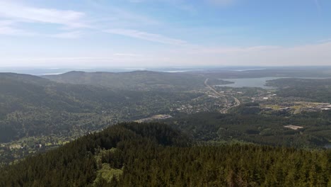 Vista-Aérea-Panorámica-En-La-Cima-De-La-Montaña-Con-Vista-Al-Bosque-Siempre-Verde-Y-La-Ciudad-Al-Fondo-En-El-Estado-De-Washington