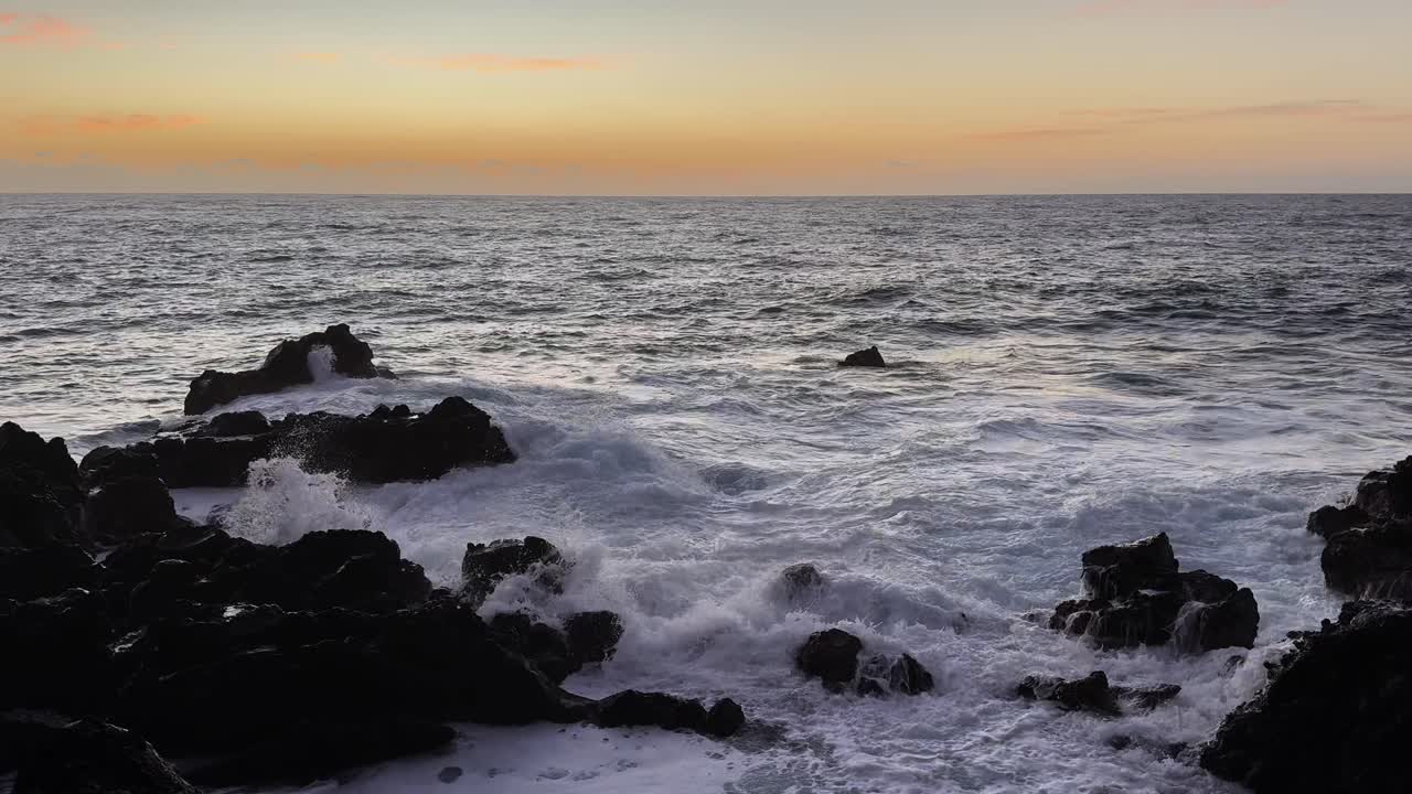 Sterke havbølger som slår mot steiner i skumringen på Hawaii