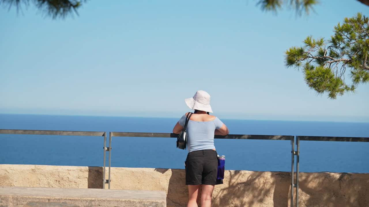 A traveler girl in a white bucket hat takes in the coast from a breezy hilltop lookout in Alicante, Spain