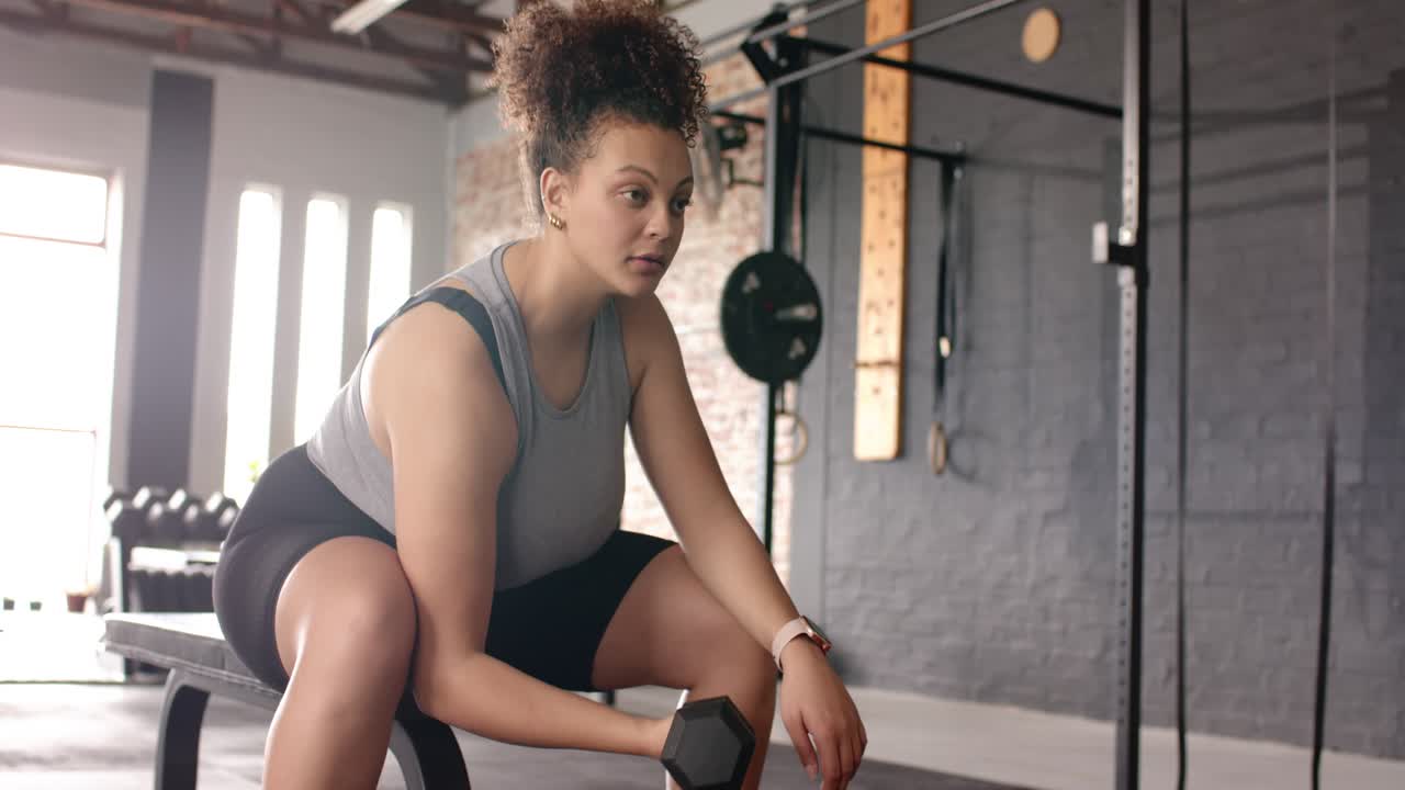 Seorang wanita mengangkat dumbbell hex di bangku di gym melakukan curl lengan kanan untuk membentuk otot