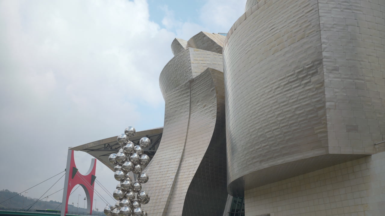 Titanium Museum Facade With Red Bridge And Reflective Sphere Sculpture, Curved Panels Catching Soft Overcast