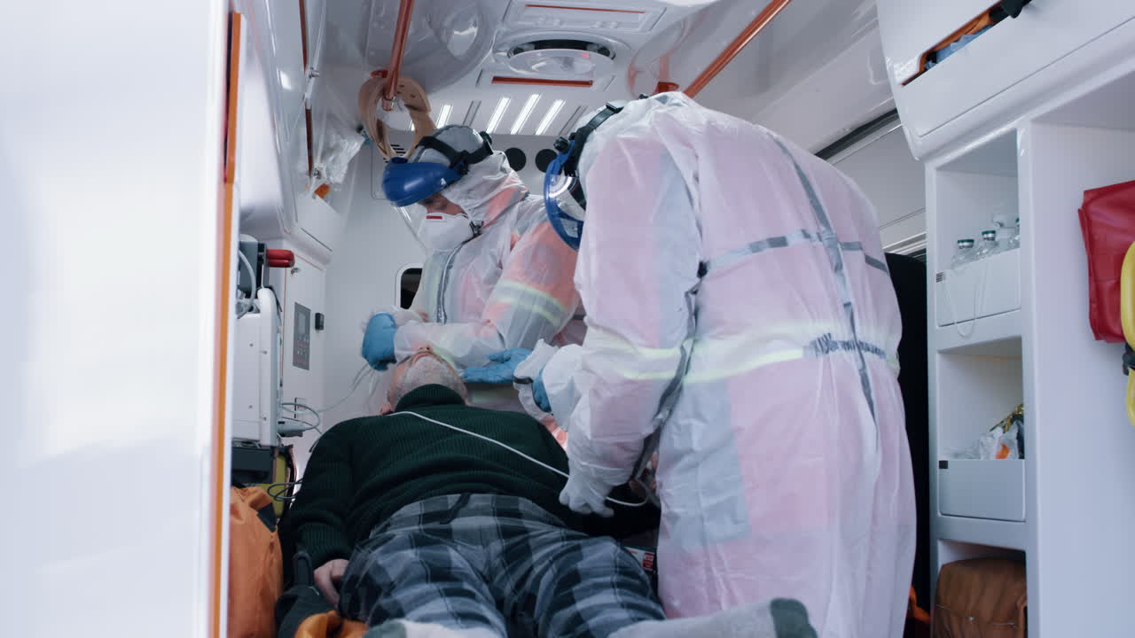 emergency Medicine Workers with Patient in Ambulance Paramedics in Hazmat Suits Putting Oxygen Mask on Aged Man while Taking Care of Patient in 911 Service Vehicle