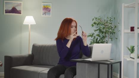 Freelancer-with-red-hair-sits-on-sofa-putting-on-glasses