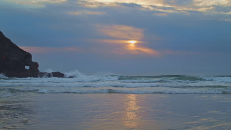 los surfistas montan olas nocturnas mientras el sol brillante se desvanece en las nubes sobre la playa