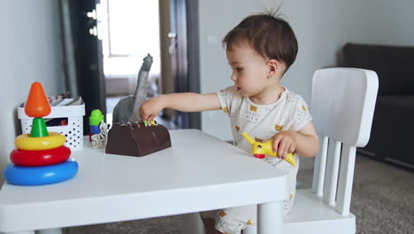 happy active toddler plays at the little desk. kid takes plastic bird and bangs it by the table.