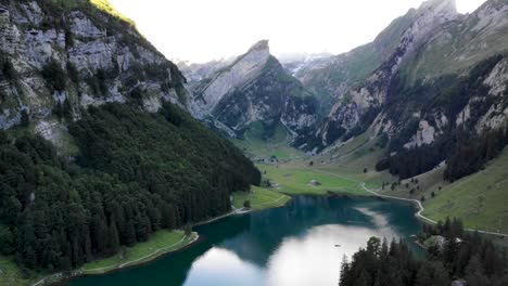 Aerial-flyover-down-towards-the-water-of-lake-Seealpsee-in-Appenzell,-Switzerland-with-a-reflection-of-the-Alpstein-peaks-on-the-lake