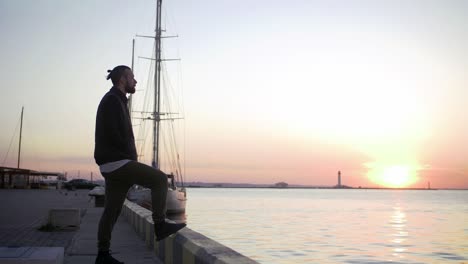 stylish hipster man on sea port background during sunset, looking aside