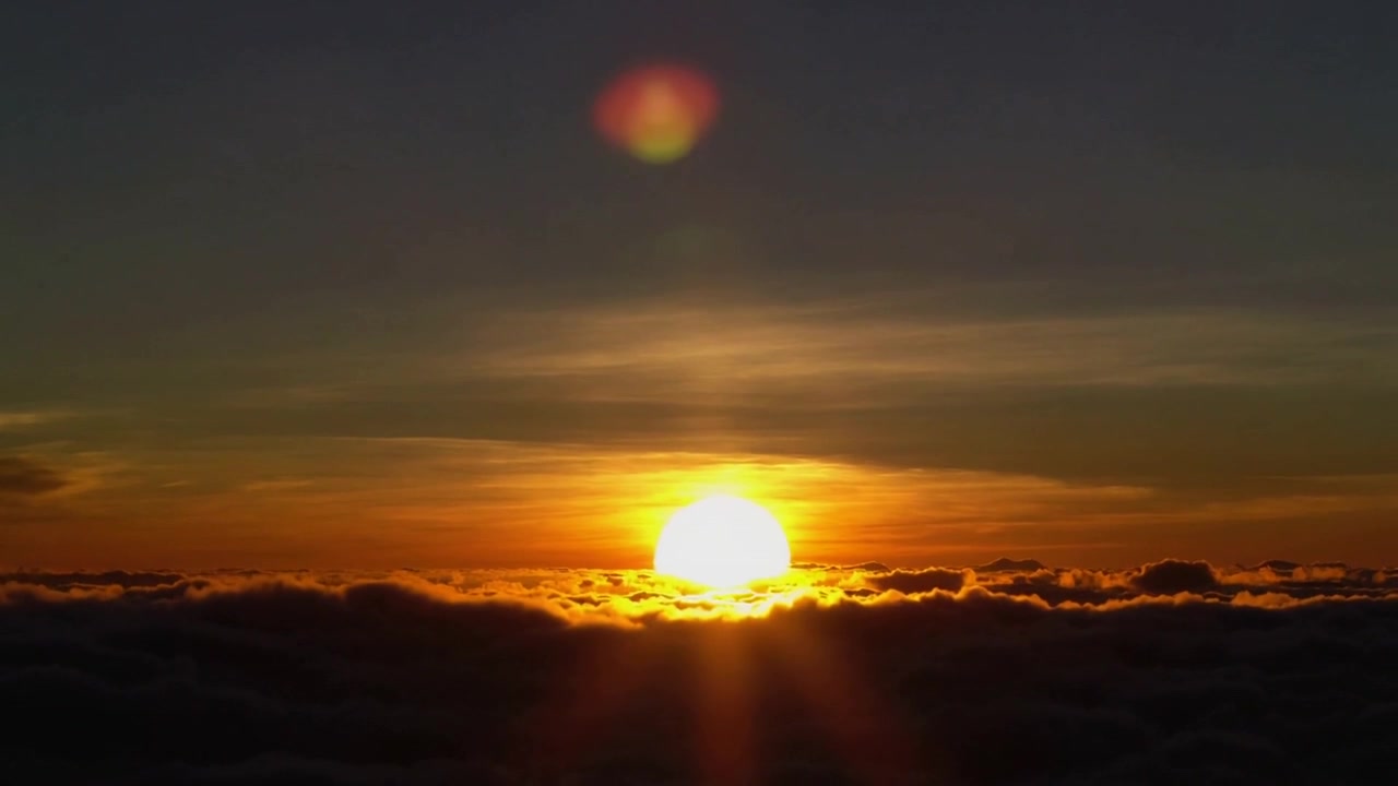 Rising sun from mountain lighting golden cloud tops above dense cloud ridge, lens flare appearing