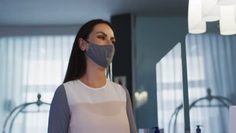 Caucasian-female-receptionist-wearing-face-mask-at-hotel-reception-desk