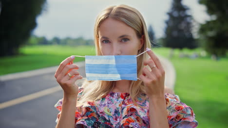 Young-woman-putting-on-medical-mask-in-garden