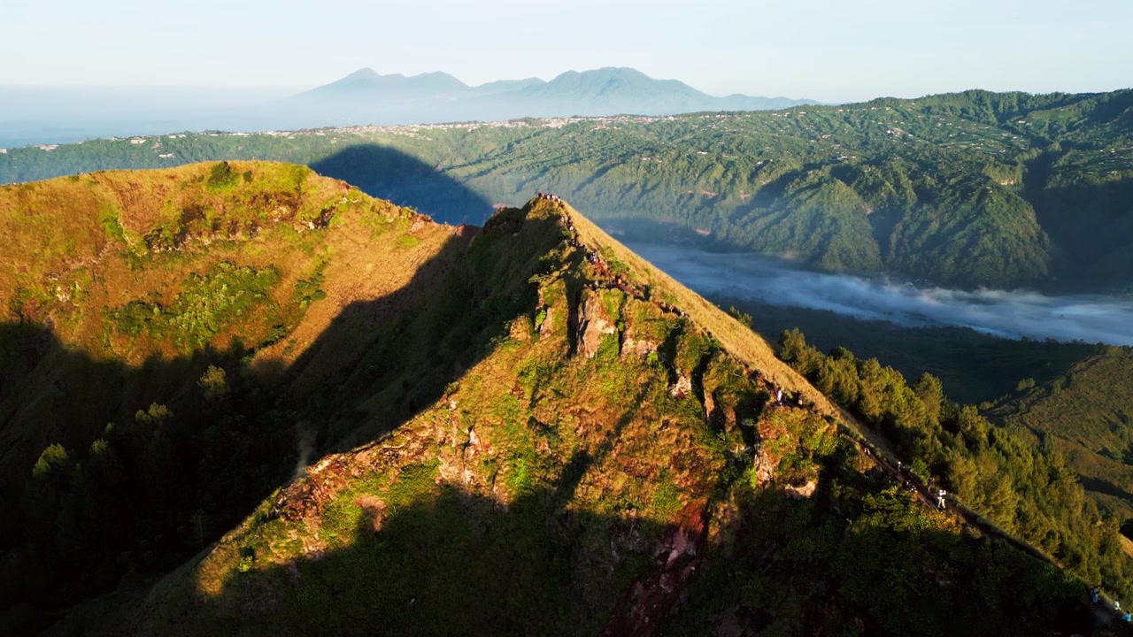 Escursionisti che camminano lungo una stretta cresta vulcanica all'alba, sentiero esposto sulla cresta con vista sulla caldera e terreno montuoso accidentato nel paesaggio di Bali, Indonesia, riprese aeree con drone in ascesa.