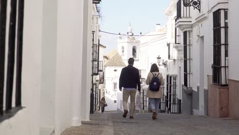 Toma-En-Cámara-Lenta-De-Una-Pareja-Caminando-Por-Un-Pequeño-Callejón-Con-Pequeños-Apartamentos-Blancos