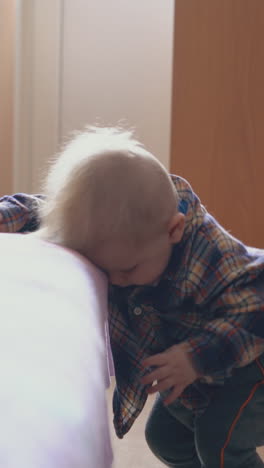 adorable fair haired baby leans on large soft bed with pink plaid in modern children room closeup