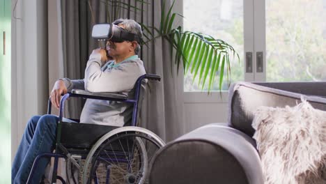 hombre mayor de raza mixta feliz en silla de ruedas con auriculares vr y divirtiéndose en casa