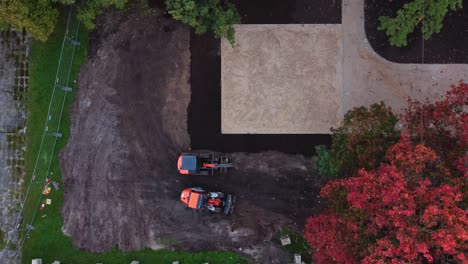 two excavators work on a construction site in riga surrounded by autumn foliage from an aerial view