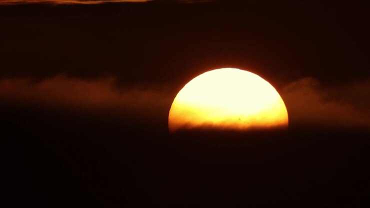 A huge yellow round sun sets behind black tense clouds