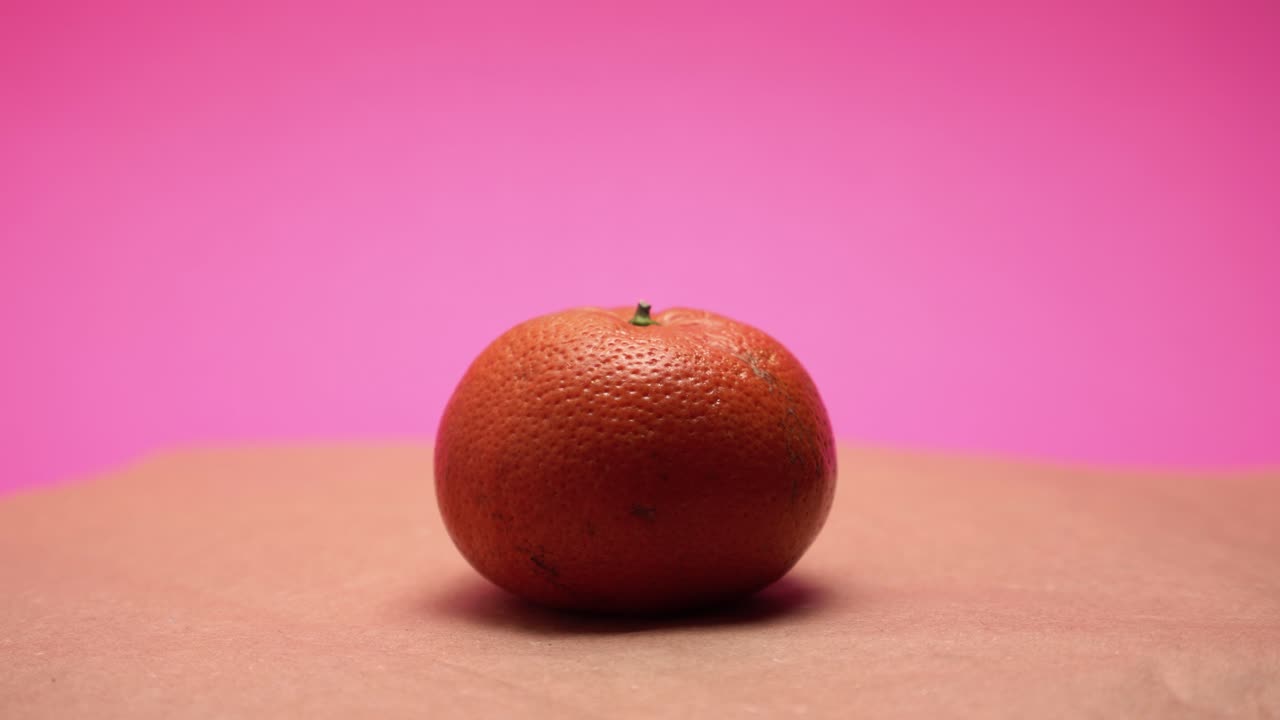 mandarina madura, gire sobre fondo de papel rosa y viejo video 4k coloreado