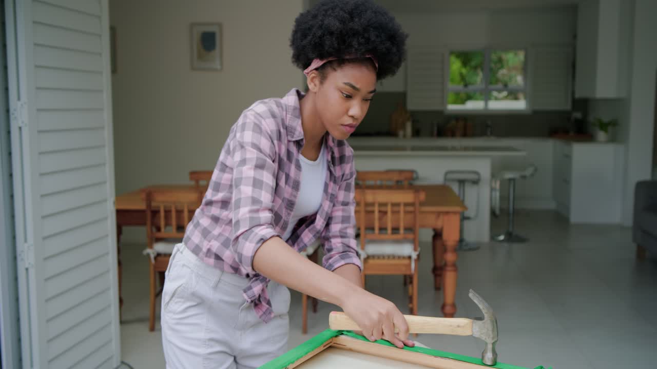 African woman finding frame hammering to secure green fabric, inspecting panel upright on worktable