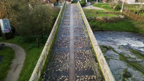 dolly sin avión sobre el puente de piedra de musgo que cruza el río lonia en ourense, españa
