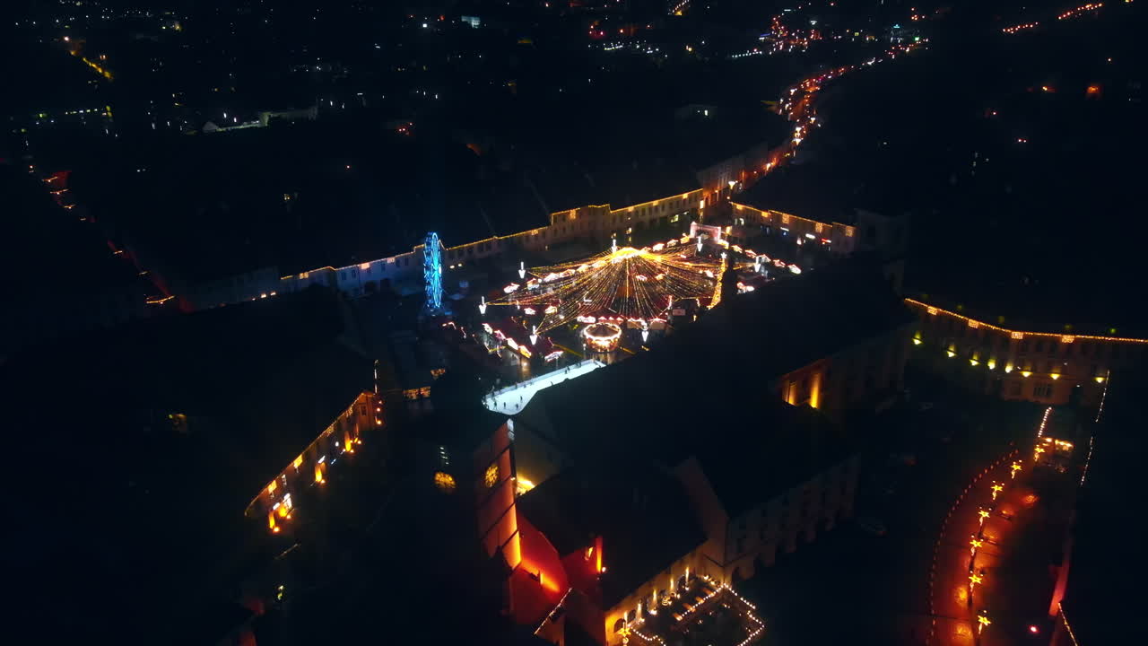 Aerial drone view of The Big Square in Sibiu at night, Romania. Old city centre decorated for Christmas. Ferris wheel, skating rink, cityscape, people