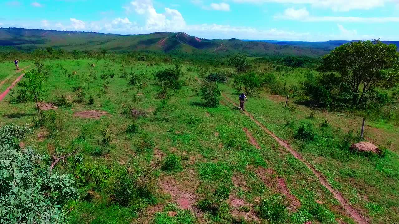 Droneoptagelse, der flyver over offroad-cyklister under et løb gennem et græsklædt landskab i Sydamerika
