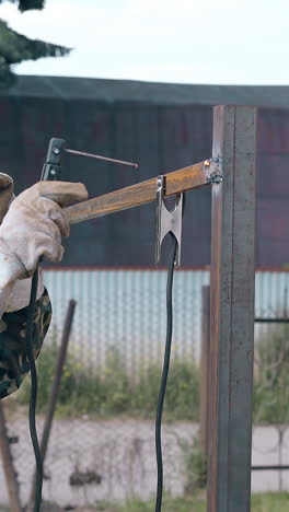 side view skilled repairman in uniform welds rusty fence carcass with powerful instrument at country house