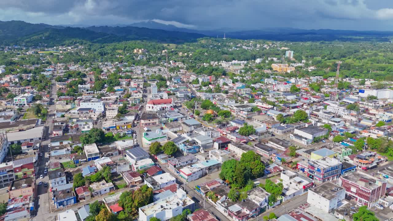 Aerial view of Cotui Cityscape with Tropical trees and colored roofs at daytime. Main street with traffic in town on Dominican Republic. Drone shot.