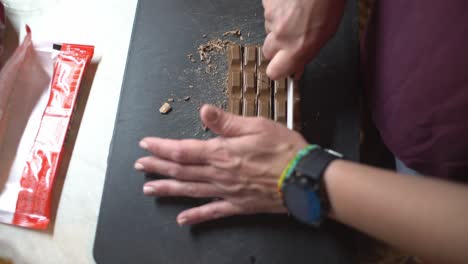 Close-up-on-woman's-hands-chopping-chocolate-,-preparing-homemade-energy-bars,-over-the-shoulder-high-view