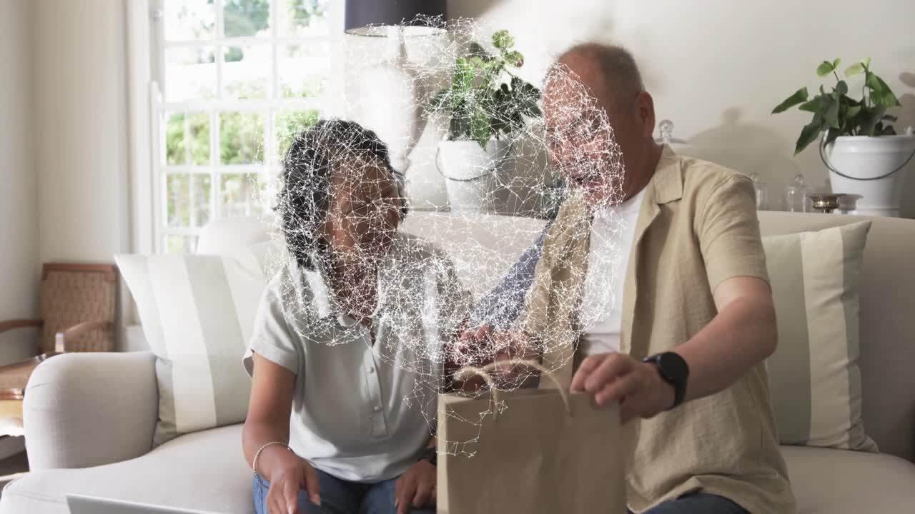 Senior woman waving at laptop causing tech globe, man entering with bag, both verifying purchase