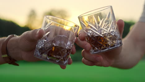 friends toast glasses outdoors. two men clinking drinks together on sunset field