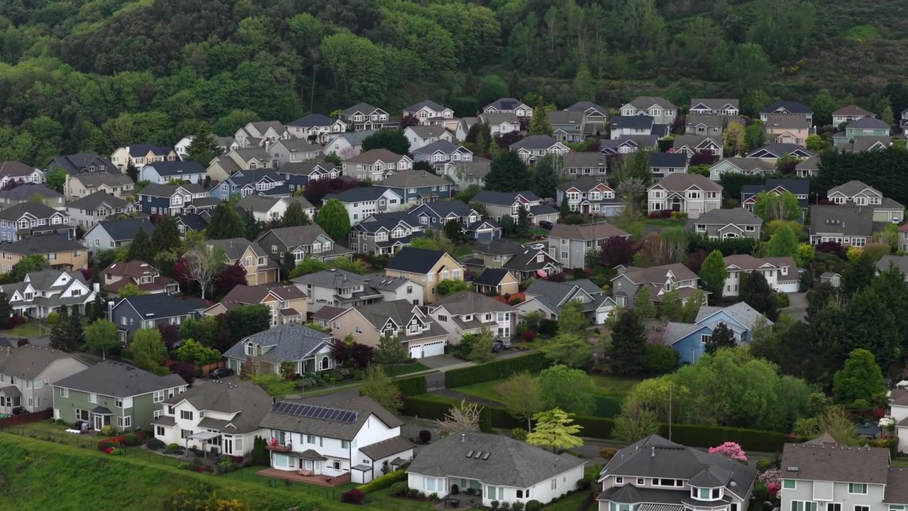 Eksklusivt forstadskvarter med store enfamiliehuse, solpaneler og velplejede haver på tværs af bølgende bakkelandskab med en tæt skovklædt højderyg i baggrunden i Tacoma, Washington, USA. Droneoptagelse