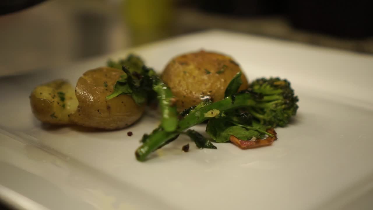 SLOW-MO - Primo piano - Mettendo broccoli freschi verdi al vapore e grigliati, spinaci, cipolla, erbe aromatiche e patate su un piatto bianco.