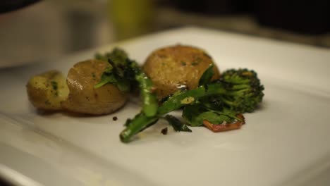 cámara lenta - primer plano - poner brócoli verde, espinacas, cebolla, hierbas y patatas frescas al vapor a la parrilla en un plato blanco