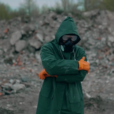 survivor in post-apocalyptic zone. man in green safety suit and gas mask and safety gloves standing in ruined place and pointing his finger on camera