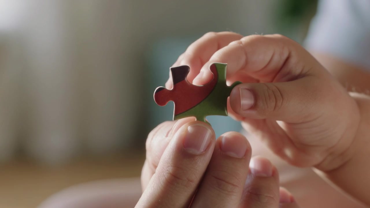 Adulto con maglietta grigia che offre un pezzo di puzzle a casa, bambino piccolo che si allunga, imparando a incastrare.