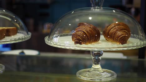 two fresh croissants under a glass dome in a bakery