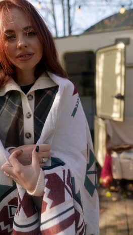 woman wrapped in blanket, smiling by a camper van in autumn