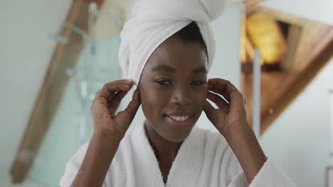 Smiling-african-american-attractive-woman-putting-towel-on-head-and-looking-at-mirror-in-bathroom