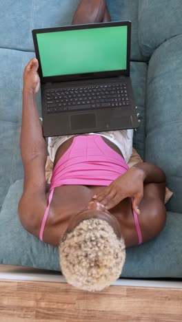 person lying on couch using laptop with green screen