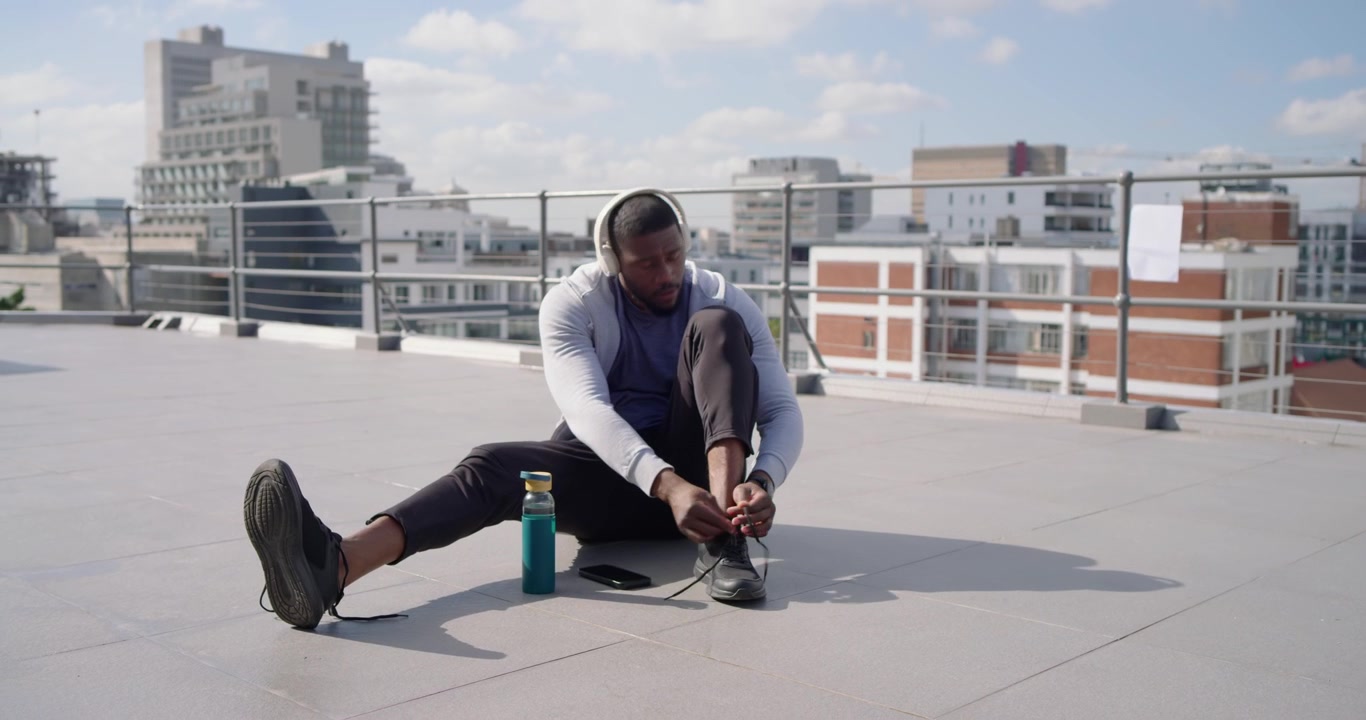 Man putting on headphones after checking phone and tying laces on rooftop preparing workout
