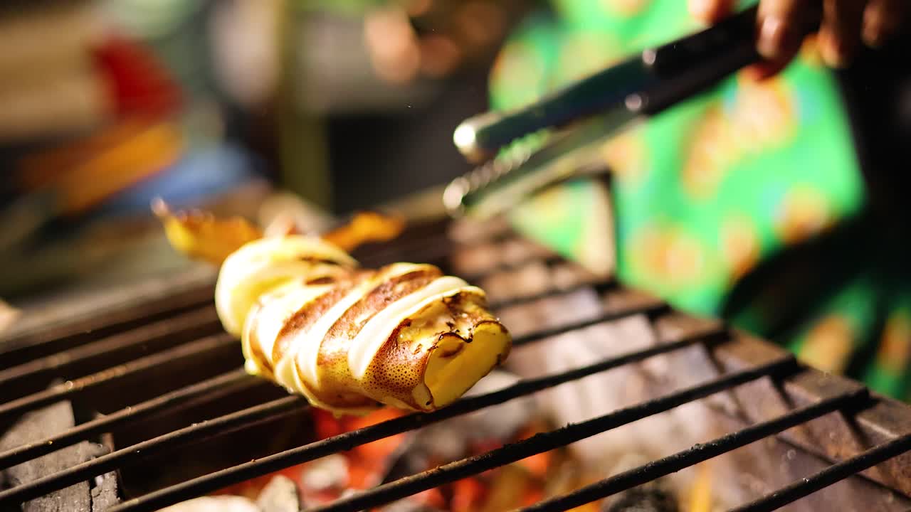 Vendor grills and turns whole squid over open flame, vibrant street food scene, shallow depth