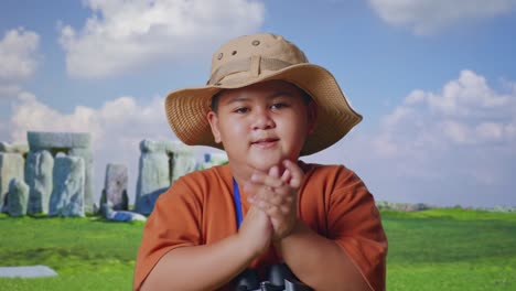 asian boy with a hat clapping hands after looking through the binoculars. boy researcher examines something while traveling in stonehenge, travel tourism adventure concept, close up