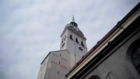 a dramatic low-angle shot of st. peter’s church tower in munich, germany. the historic clock tower stands against a cloudy sky, showcasing its architectural details and european charm.