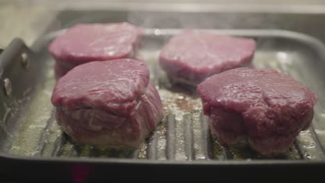 closeup on four steaks in a frying pan being cooked in oil