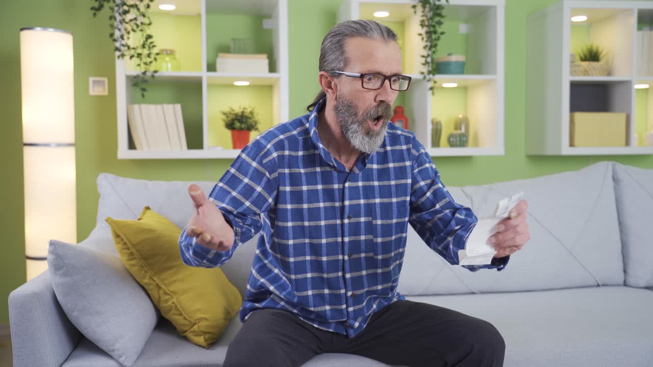 hombre de mediana edad enojándose en casa con una factura de alto precio.