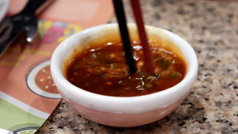 mixing some spicy sukiyaki sauce with a pair of chopstick in a small dipping bowl, in a restaurant in bangkok, thailand