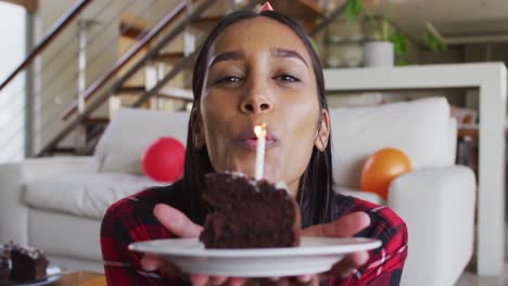 mixed race woman using laptop having birthday video chat holding a cake blowing candle